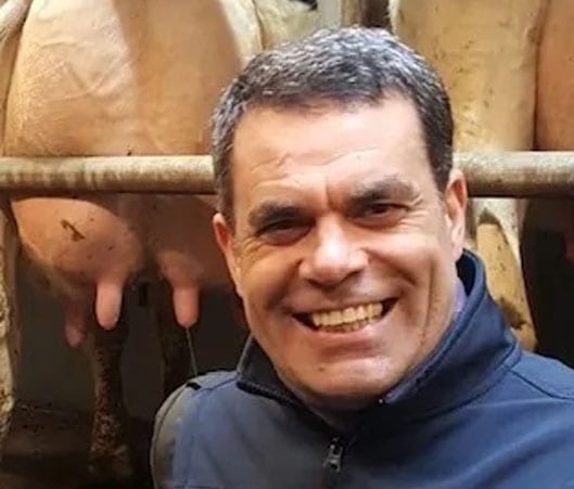 A man smiling for the camera with some cows in the background.